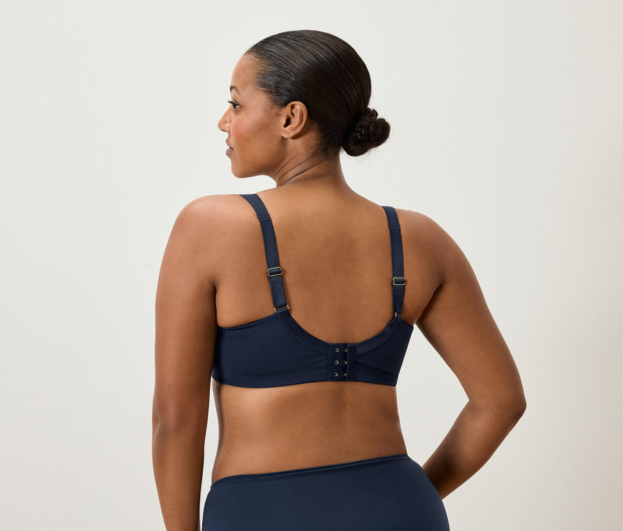 Pohľad zozadu na ženu s drdolom, ktorá má na sebe tmavomodrú podprsenku a nohavičky.