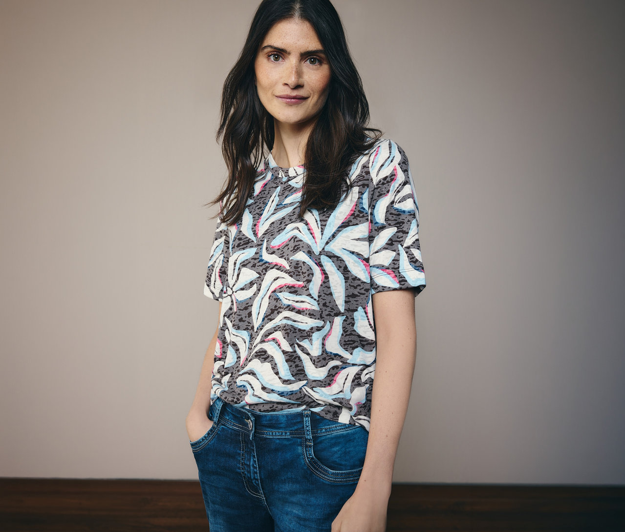 Tmavovlasá žena má na sebe modré tričko s krátkym rukávom CECIL so vzorom a modré džínsy.