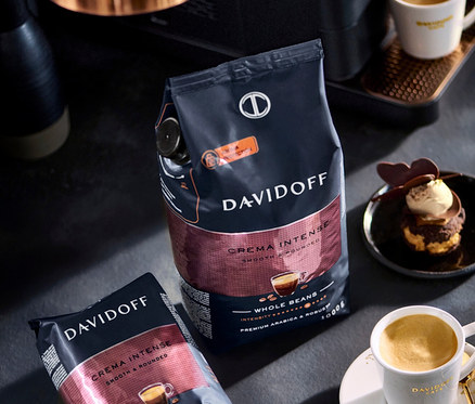 Dve balenia kávových zŕn Davidoff Crema Intense, šálka kávy a dezert na stole.
