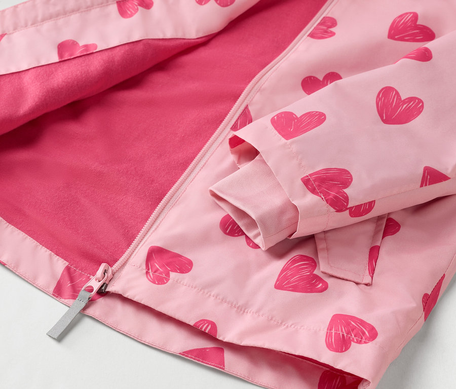 Detail otvorená, svetloružová detská bunda so vzorom červených srdiečok so zipsom po celej dĺžke.