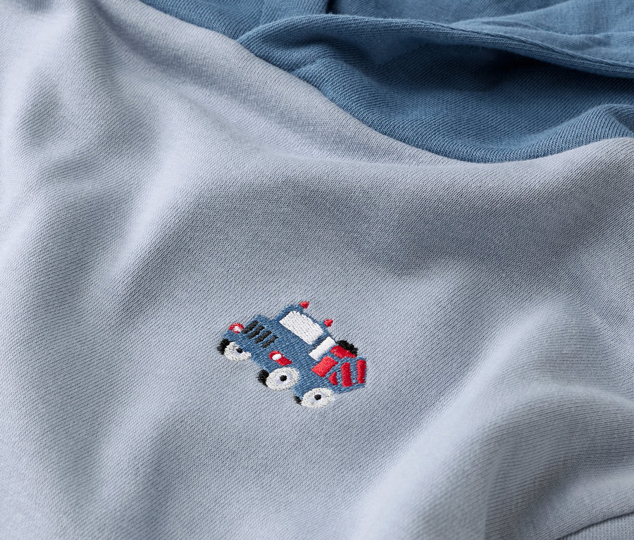 Detailný záber na svetlomodrú mikinu s tmavomodrým rukávom a aplikáciou modrého auta.