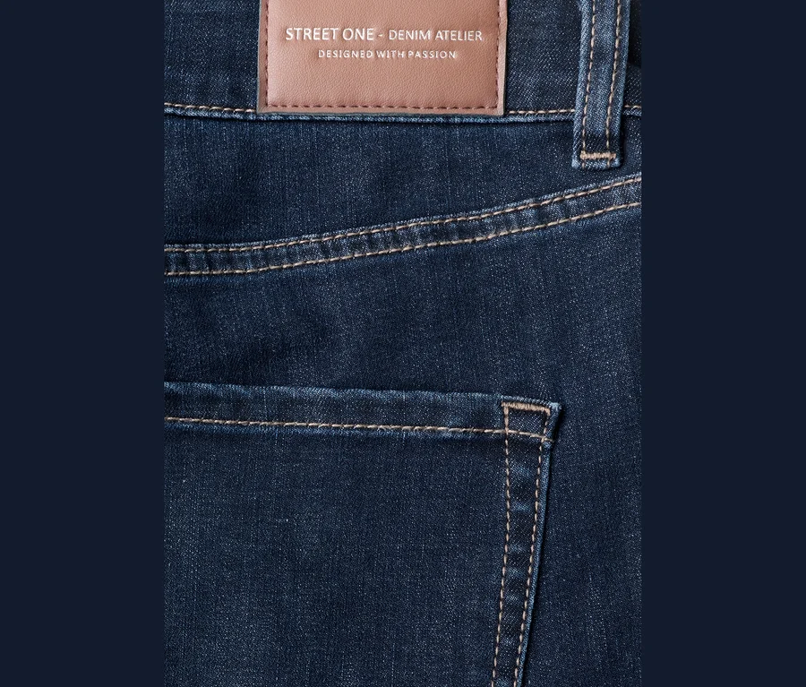 Tmavomodré džínsy Street One so svetlohnedým prešívaním a hnedou koženou nášivkou s nápisom „STREET ONE - DENIM ATELIER“ na páse.
