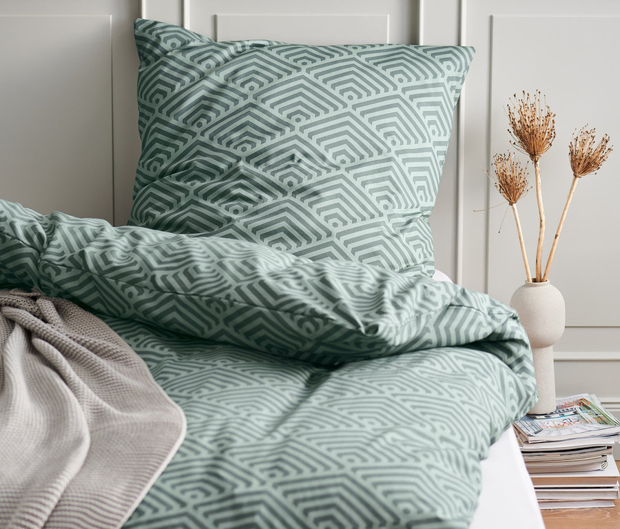 Posteľná bielizeň s geometrickým vzorom na posteli, v pozadí stena.