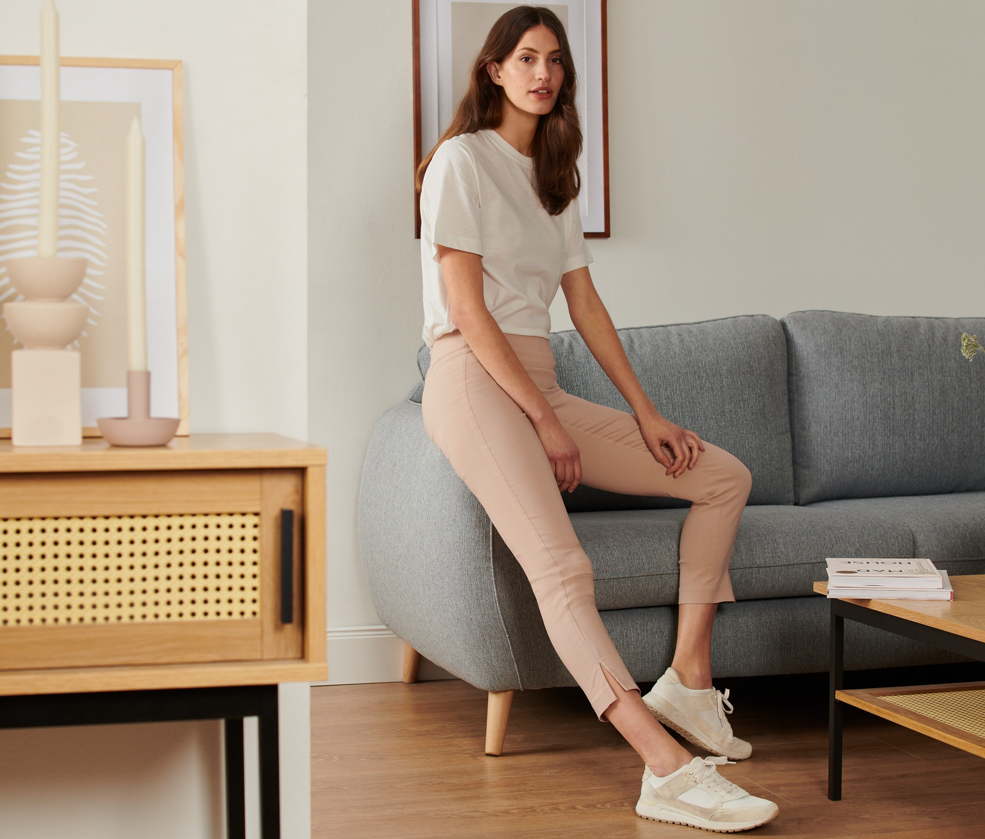 Žena sedí na sivej pohovke a má na sebe elastické nohavice.