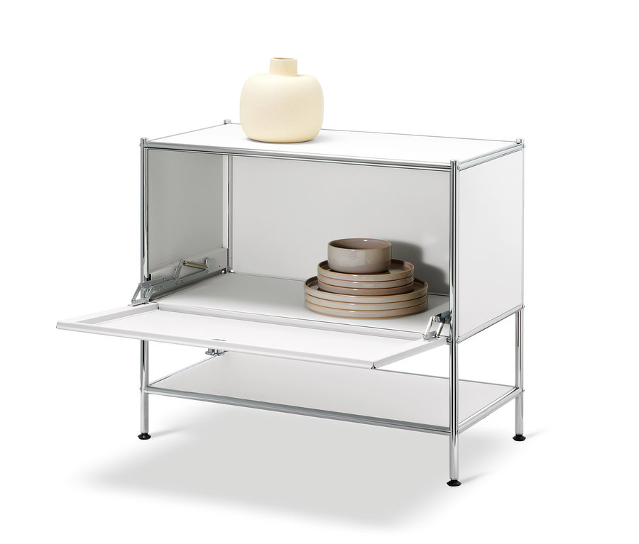 Biela odkladacia skrinka »CN3« s otvorenými výklopnými dvierkami. Na hornej polici je béžová váza, vo vnútri skrinky je sada tanierov a misiek.