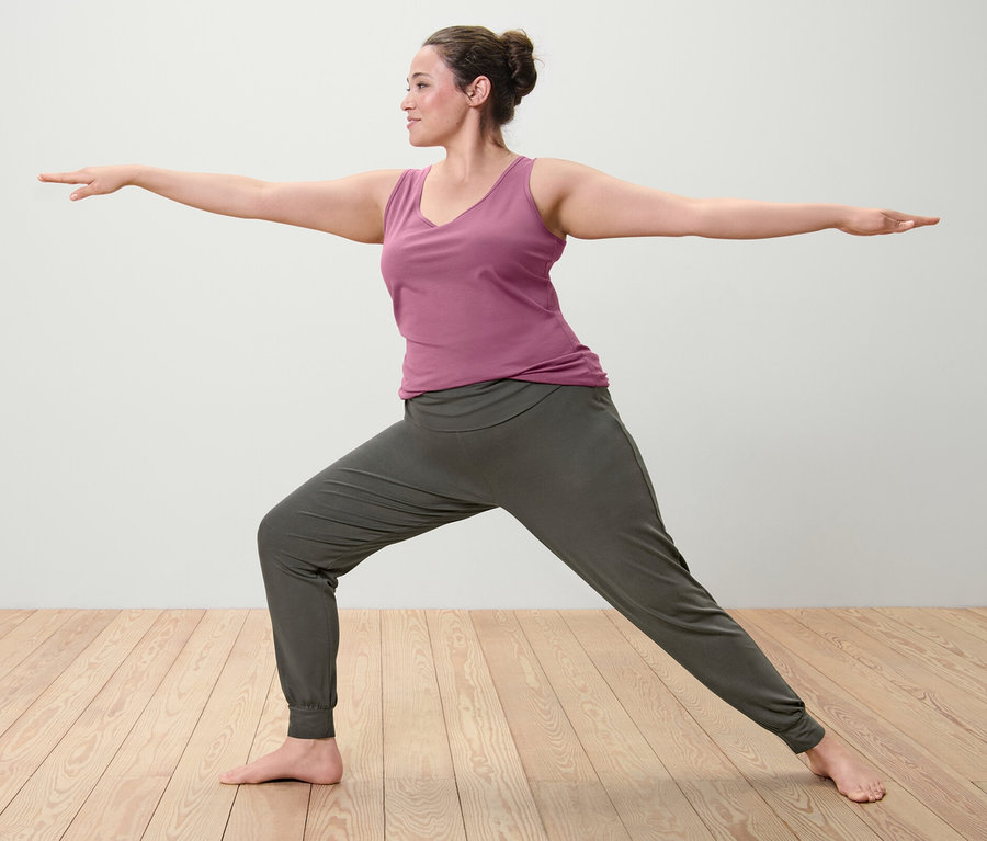 Žena v pozícii bojovníka v ružovom tielku (2 ks) a nohaviciach na jogu.