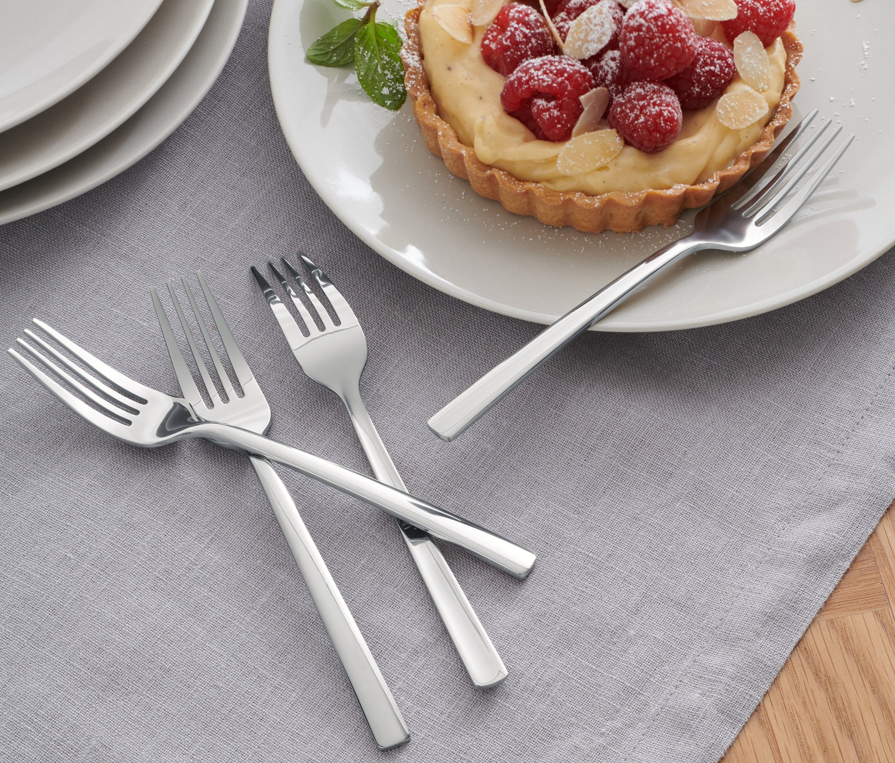 Tri zo 4 dezertných vidličiek ležia na sivom obruse vedľa taniera s malinovým koláčom.
