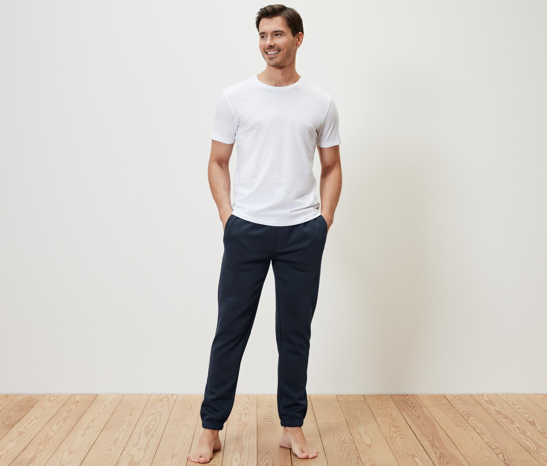 Muž stojí a má ruky vo vreckách teplákových nohavíc.