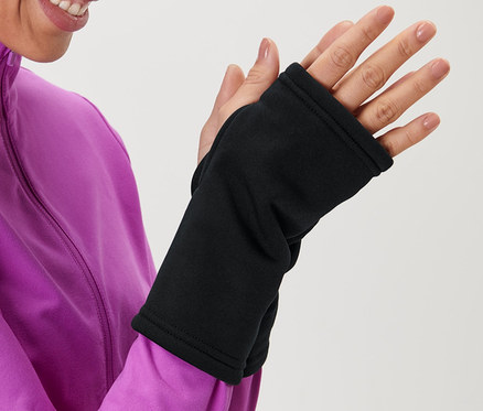 Žena v ružovej bunde si oblieka čierne návleky na ruky.