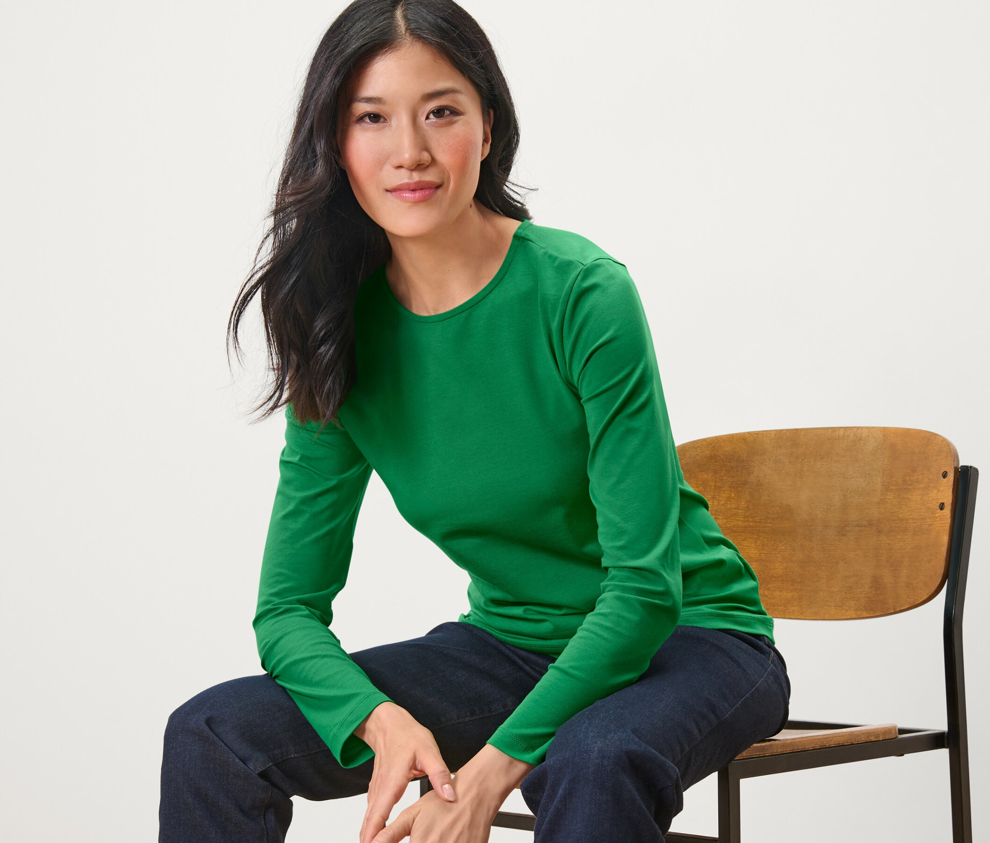 Žena sedí na stoličke a má na sebe zelené tričko s dlhými rukávmi.
