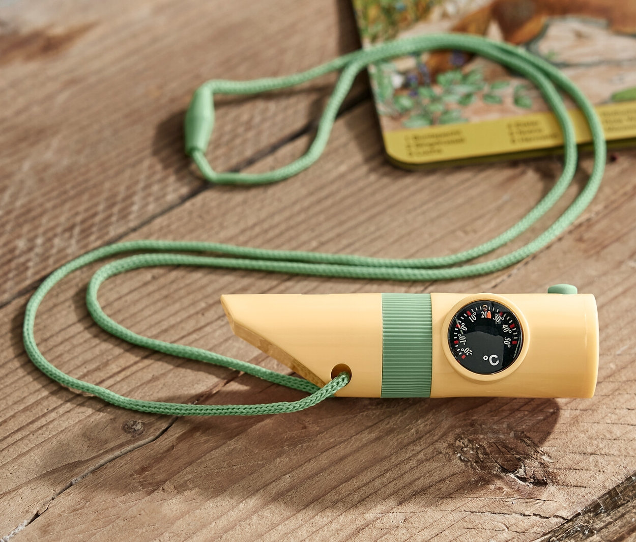 Žltý kompaktný outdoorový nástroj so zelenou šnúrkou leží na drevenom stole.