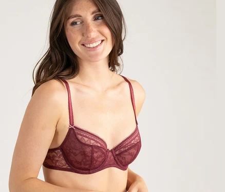 Usmievavá žena s dlhými vlasmi má na sebe bordovú čipkovanú podprsenku s polovičnými košíčkami Passionata »Jeanne«.