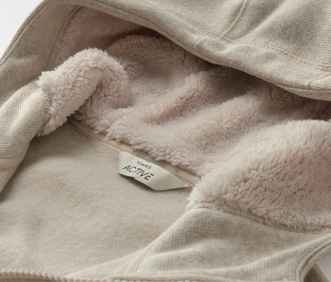 Detail béžovej mikiny s kapucňou s flísovou podšívkou a štítkom s nápisom ACTIVE.