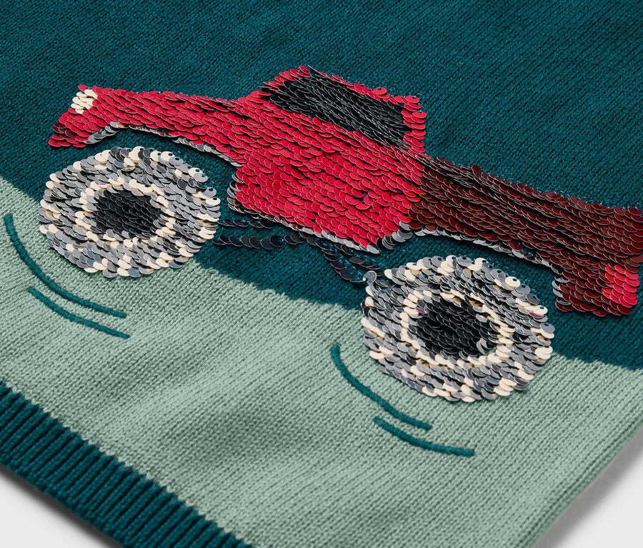 Detail detského pleteného svetra s nášivkou červeného monster trucku.