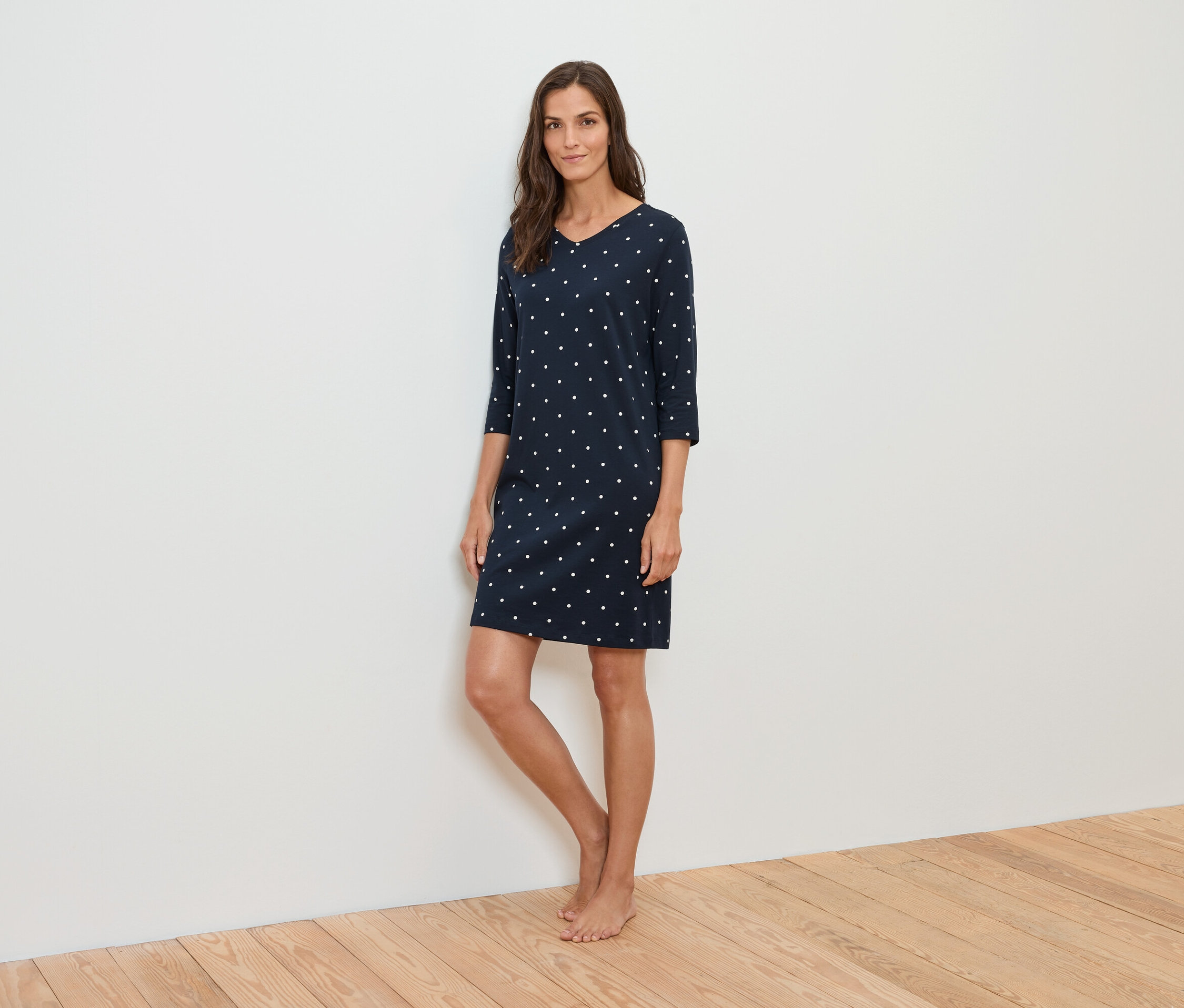 Žena stojí a má na sebe tmavomodré šaty s bielymi bodkami.