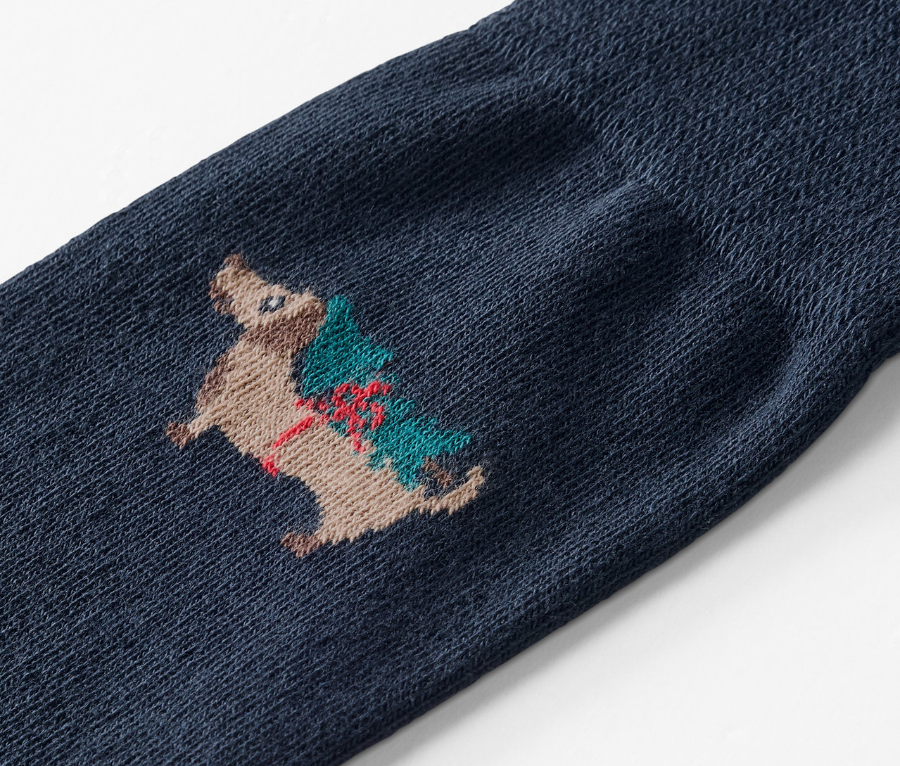 Detail modrej ponožky s výšivkou ježka nesúceho vianočný stromček.