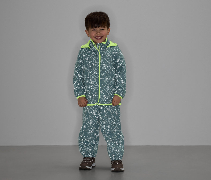 Chlapec v sivej bunde a nohaviciach so vzorom medveďa a neónovo žltým lemovaním sa usmieva.