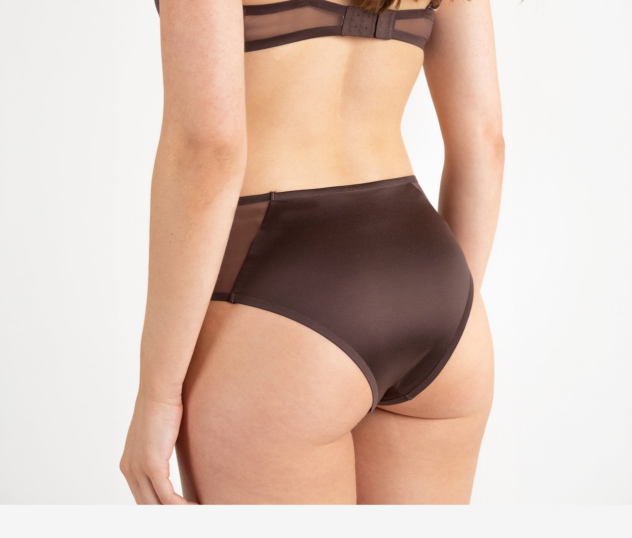 Žena zozadu v tmavohnedej podprsenke a nohavičkách Passionata High Waist Slip »Bianca« v tmavočokoládovej farbe s priehľadnými bočnými panelmi.