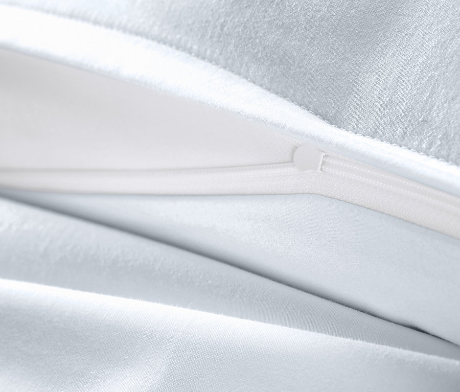 Detail bielej posteľnej bielizne z bavlny a saténu nadmernej veľkosti s otvoreným zipsom.