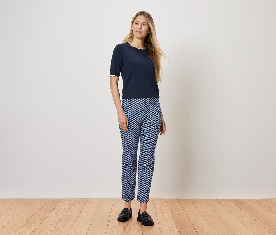 Žena stojí na drevenej podlahe a má na sebe tmavomodré tričko a modro-biele pruhované nohavice.