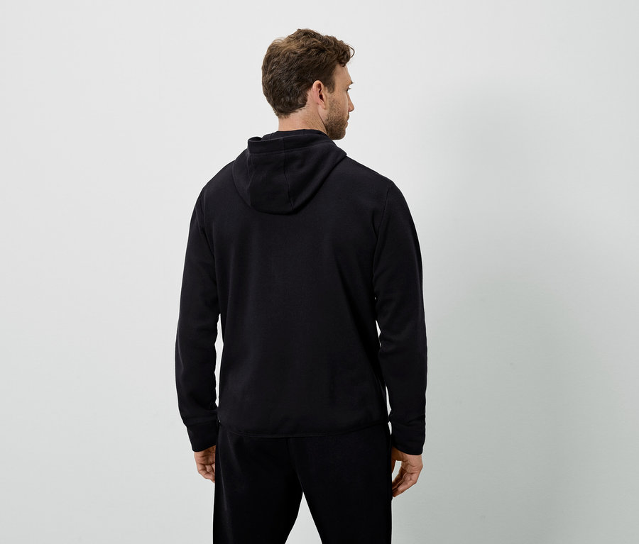 Muž chrbtom k fotoaparátu má na sebe čiernu mikinu s kapucňou a čierne tepláky.