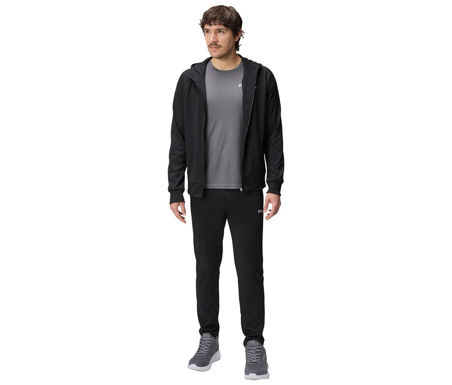 Muž v čiernej tréningovej bunde s kapucňou, sivom tričku a čiernych teplákoch a sivých športových topánkach.