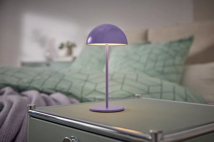Fialová lampa stojí na nočnom stolíku vedľa postele.