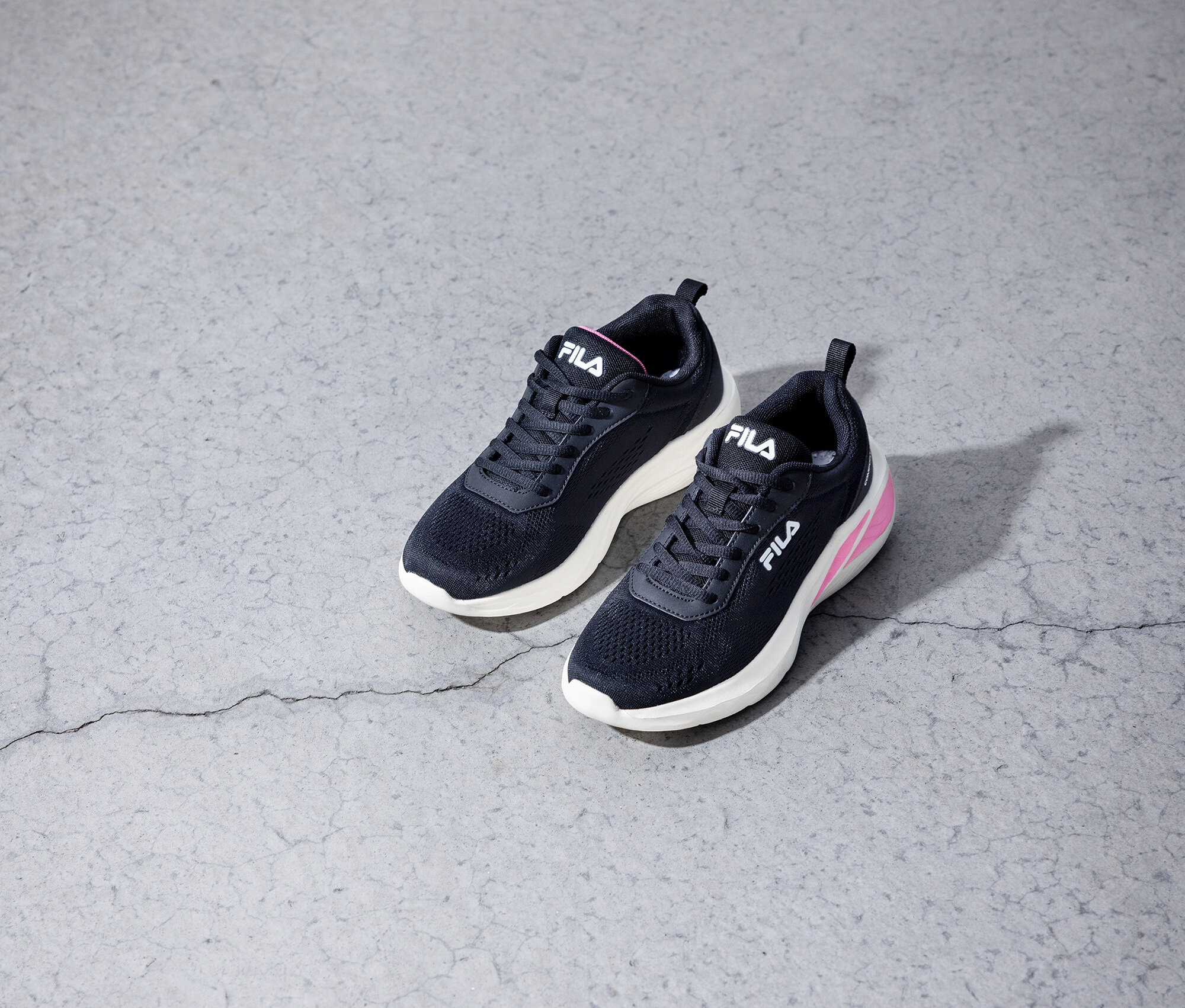 Dve čierne tenisky Fila ležia na sivej betónovej podlahe.