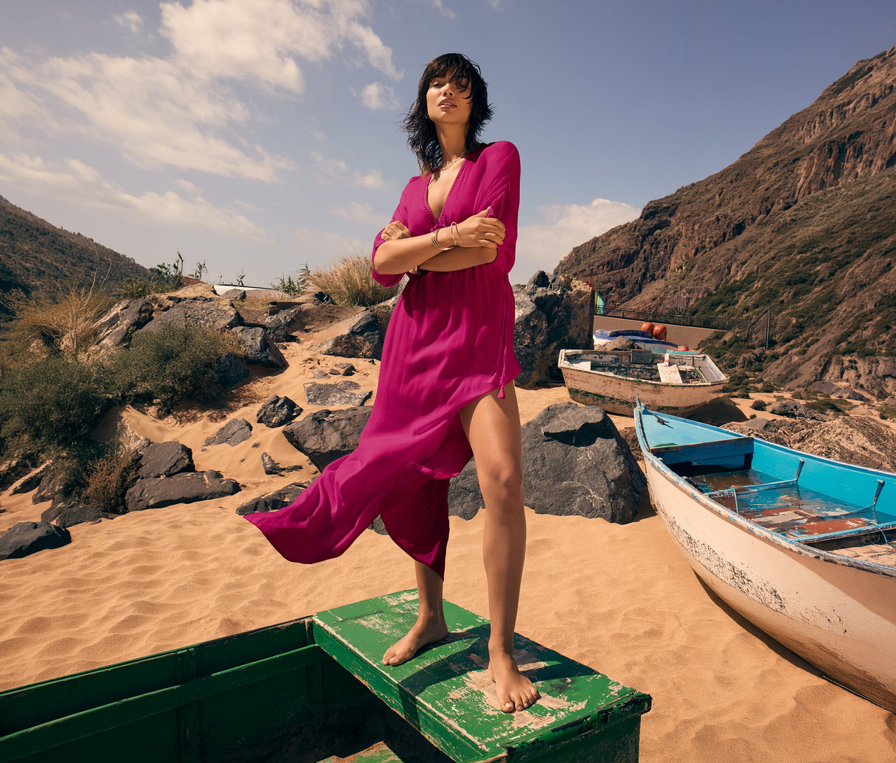 Žena stojí naboso na lodi na pláži a má na sebe Triumph Beach MyWear Kaftan Maxi Dress.