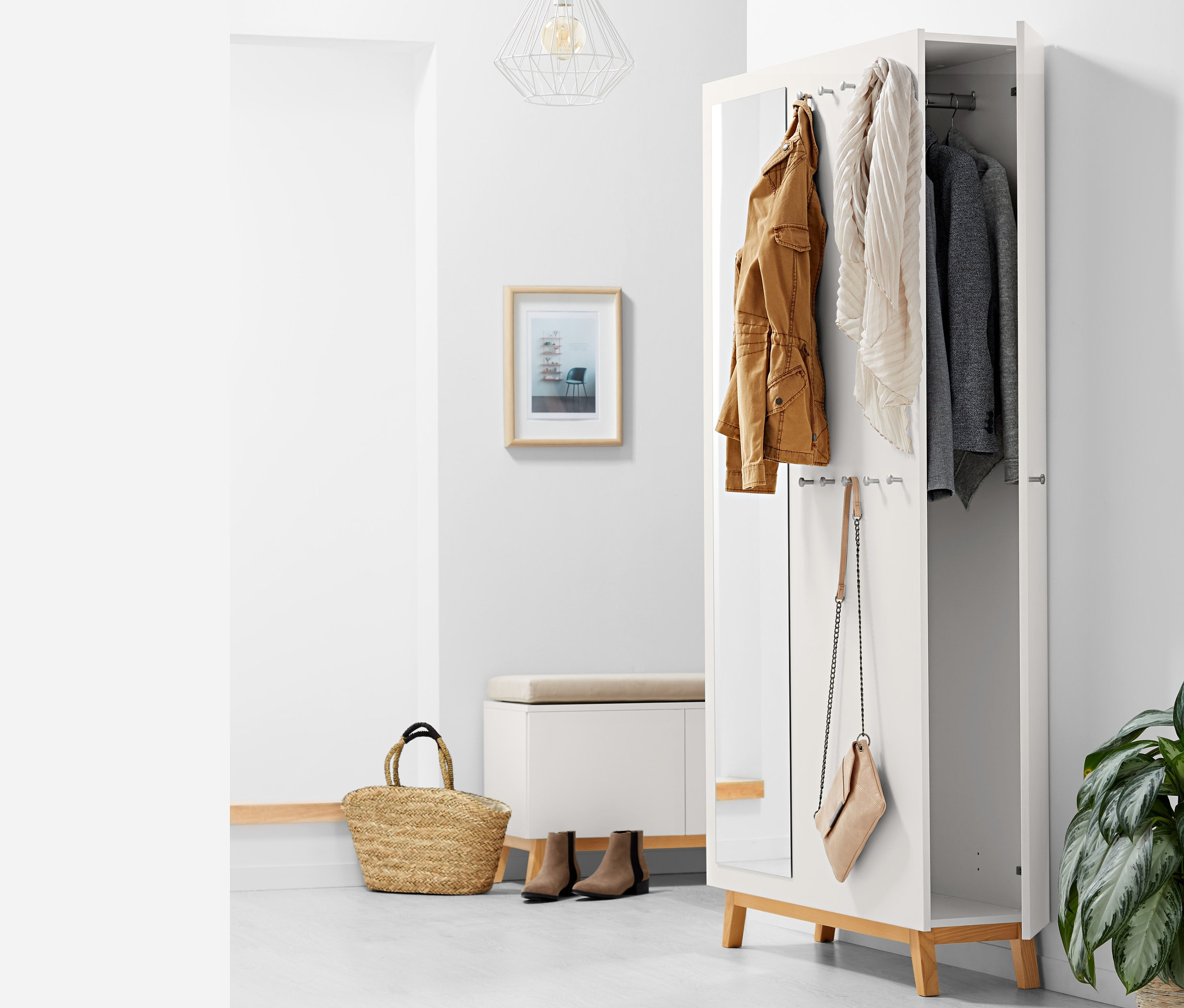 Otvorená multifunkčná skriňa do predsiene s hnedou bundou, šálom a sivým sakom visiacimi vnútri, kabelka visí na boku.