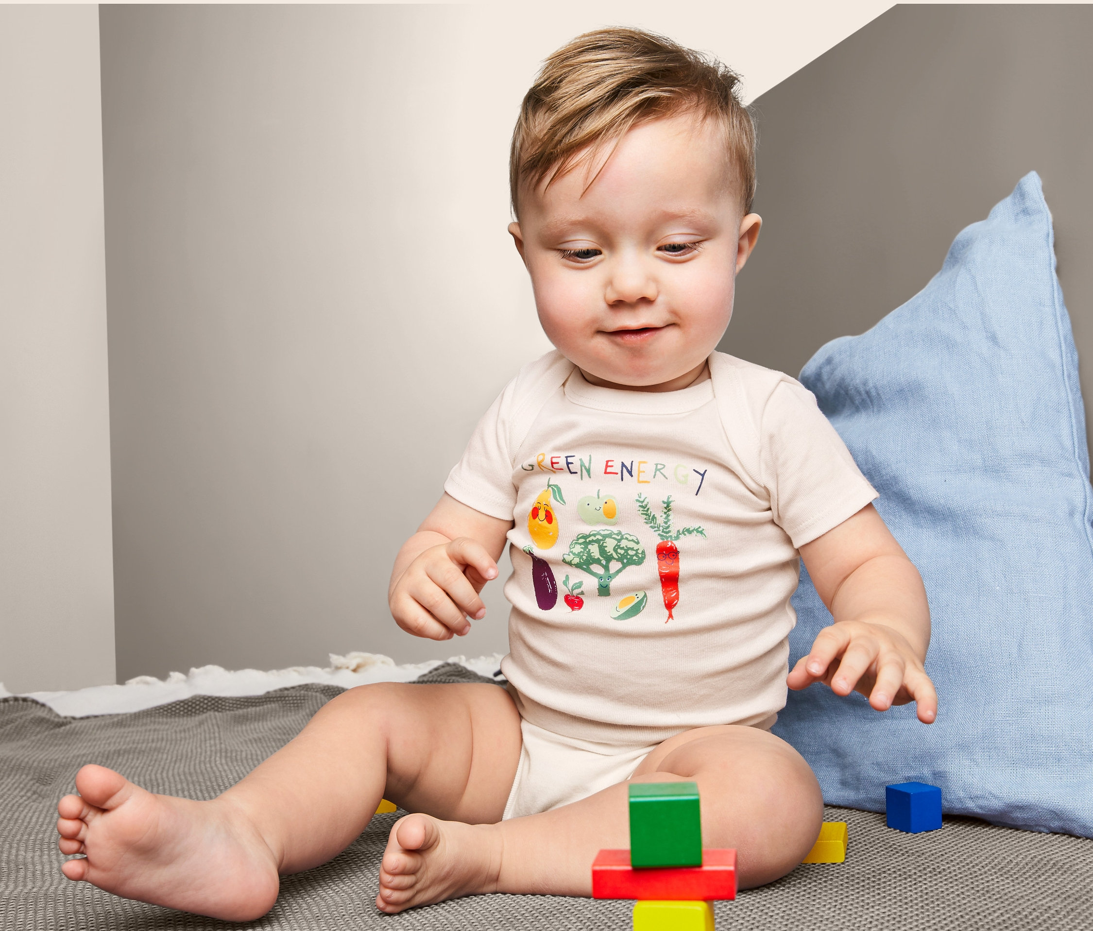 Dieťa sedí na deke a hrá sa s farebnými kockami. Má na sebe body s krátkym rukávom s potlačou zeleniny. Ide o produkt: Body s krátkym rukávom, 3 ks.