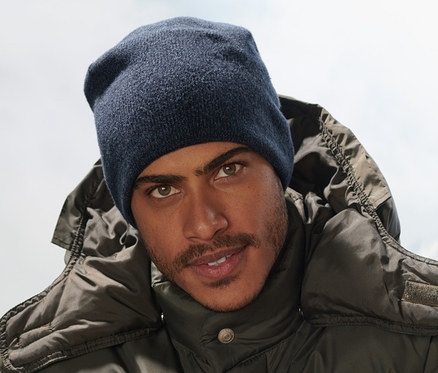 Muž sedí na lavičke a má na sebe tmavomodrú pletenú čiapku.