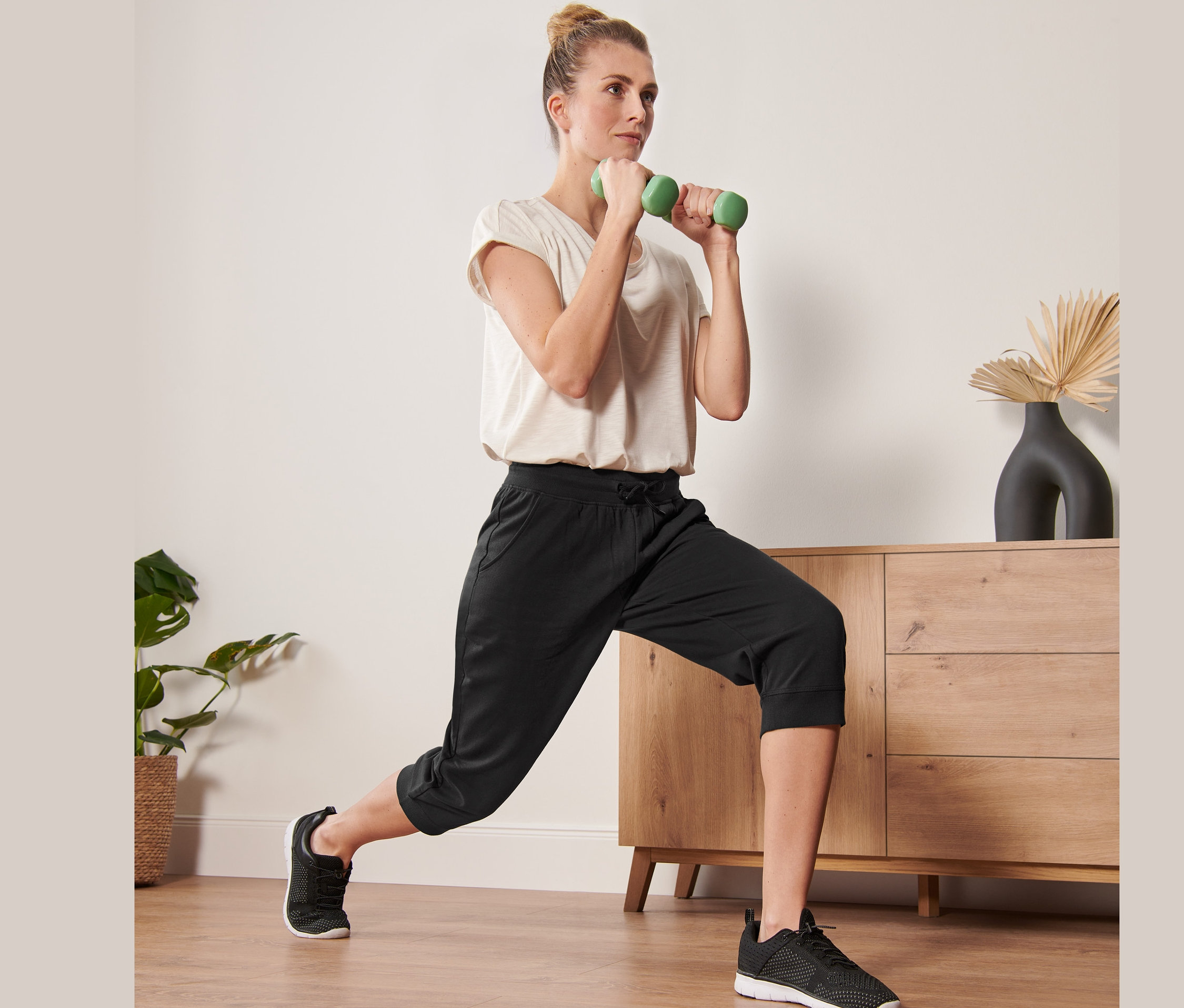 Žena cvičí so zelenými činkami v čiernych trojštvrťových športových nohaviciach.