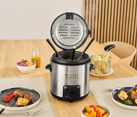 Mini fritéza a fondue na stole s jedlom na tanieroch a v miskách.