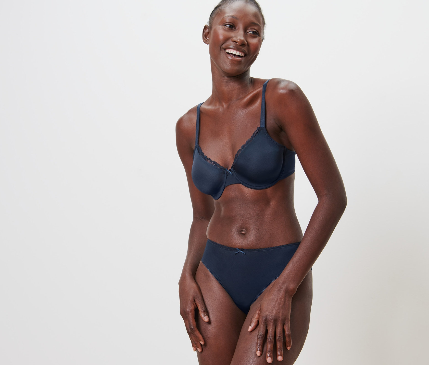 Usmievajúca sa žena pózuje v podprsenke s kosticami a nohavičkách pred bielym pozadím.