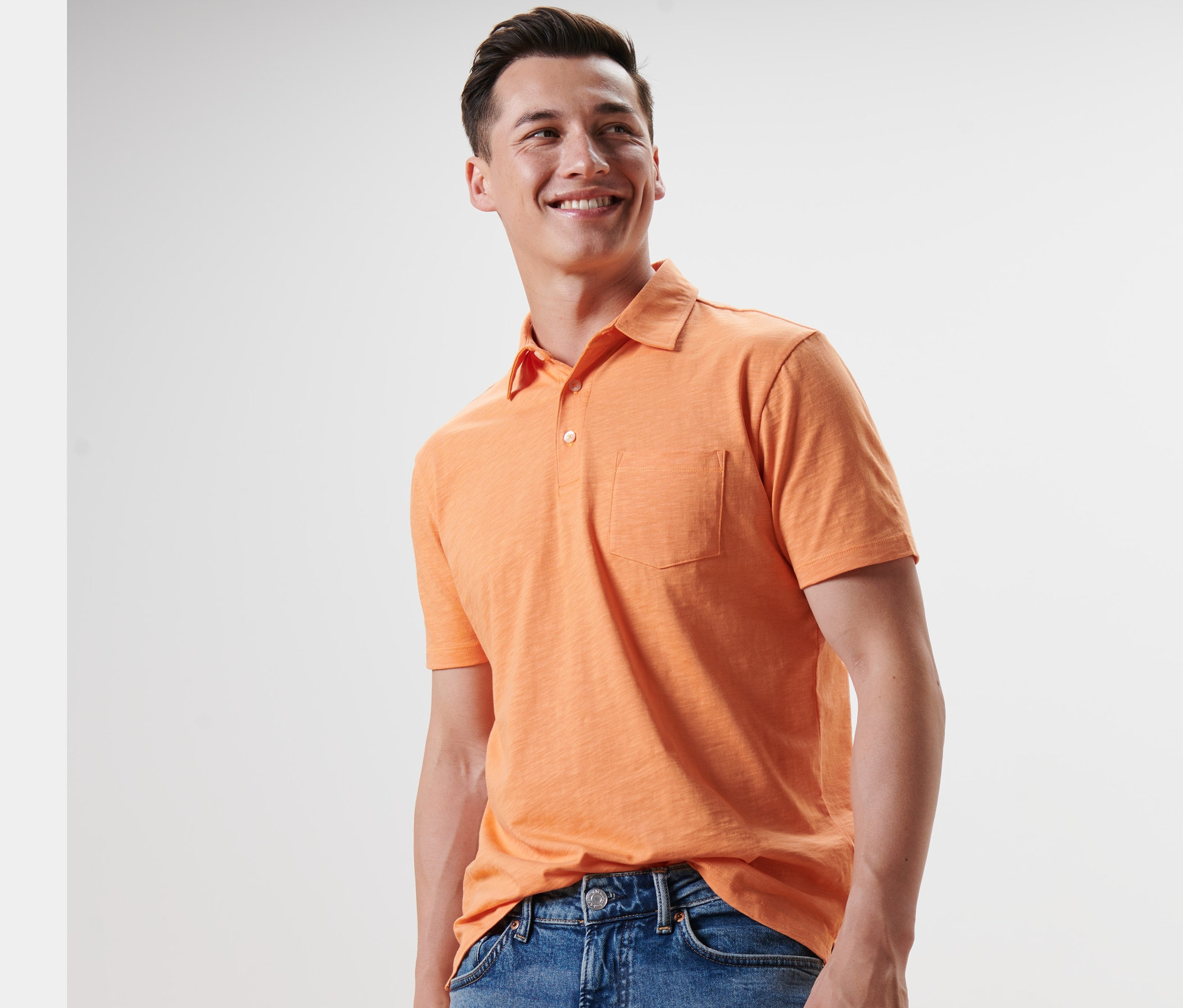 Muž sa usmieva a má na sebe oranžovú polokošeľu a džínsy.