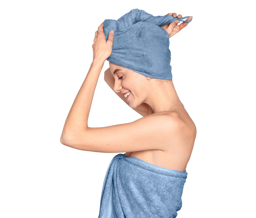 Žena si upravuje uterákový turban na hlave, telo má ovinuté uterákom.