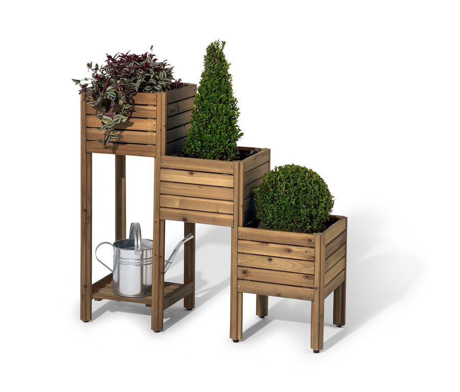 Drevený poschodový kvetináč »Tinus« s regálom naspodku s tromi rastlinami a striebornou kanvou na polievanie pod ním.