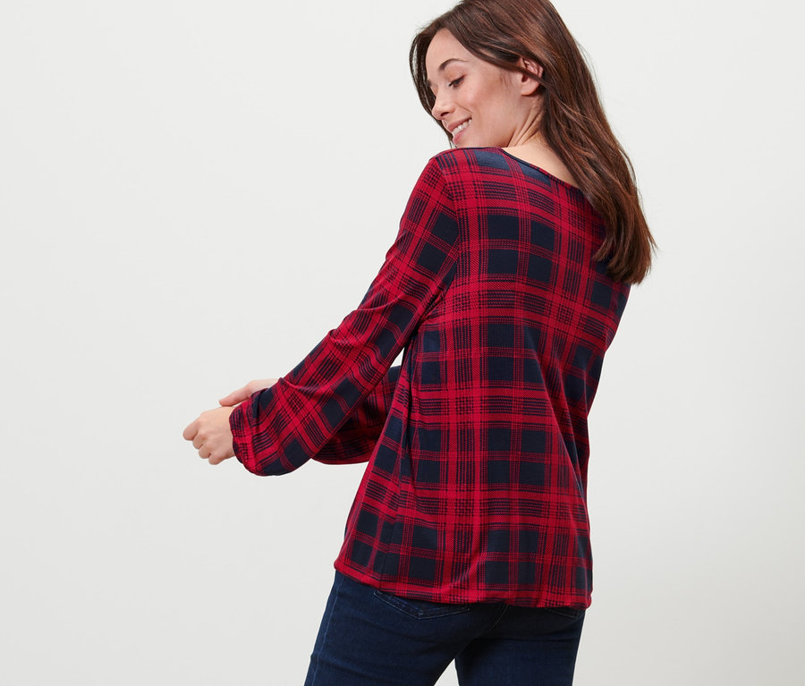 Žena sa pozerá cez plece a má na sebe kárované blúzkové tričko a džínsy.