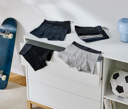 Na komode ležia pánske boxerky, vedľa nej stojí skateboard a futbalová lopta.