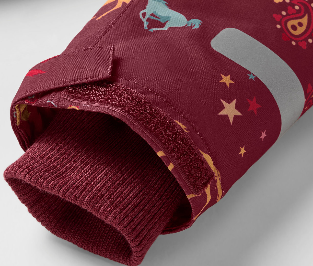 Detail bordového rukáva bundy s potlačou koní a hviezd, zakončeného bordovým lemom.