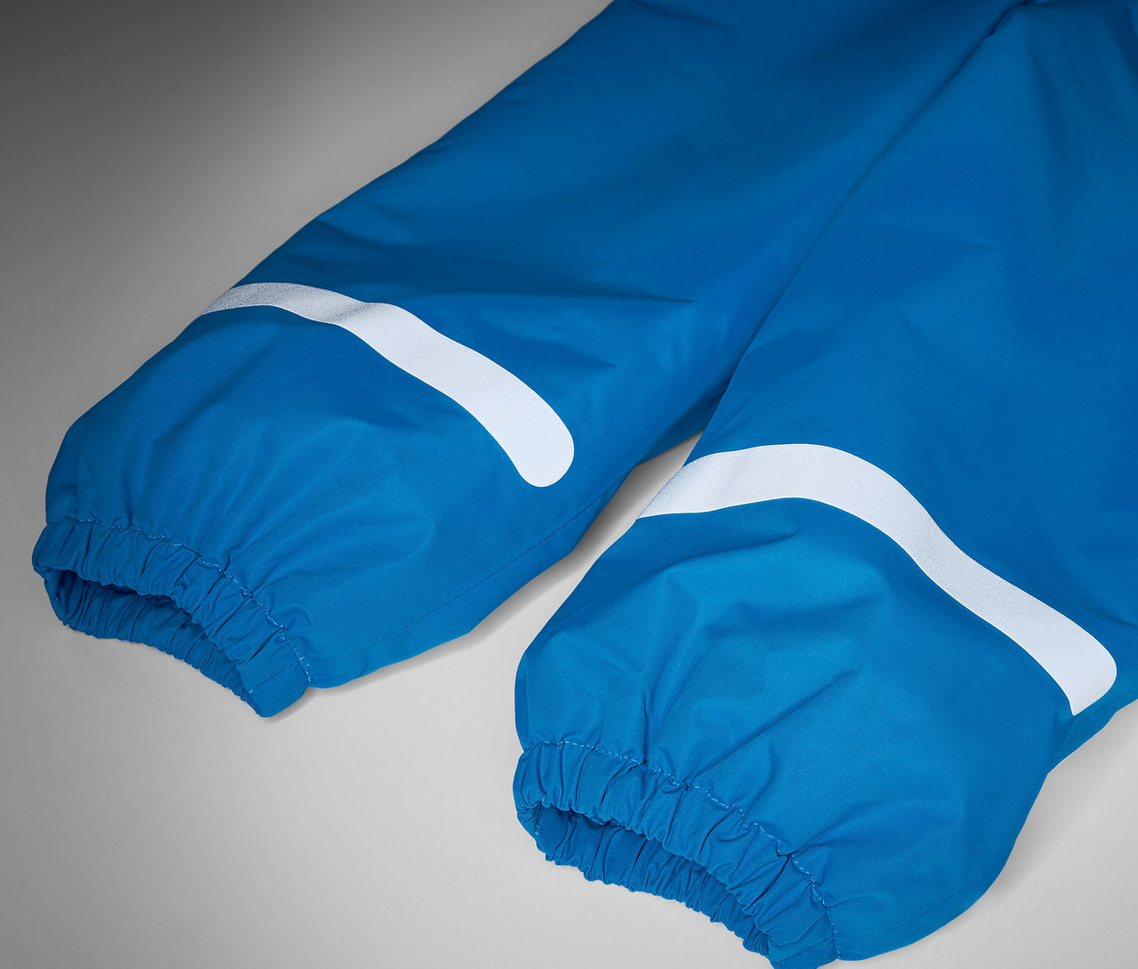 Detail modrých detských termo nohavíc do dažďa s bielymi reflexnými prvkami.