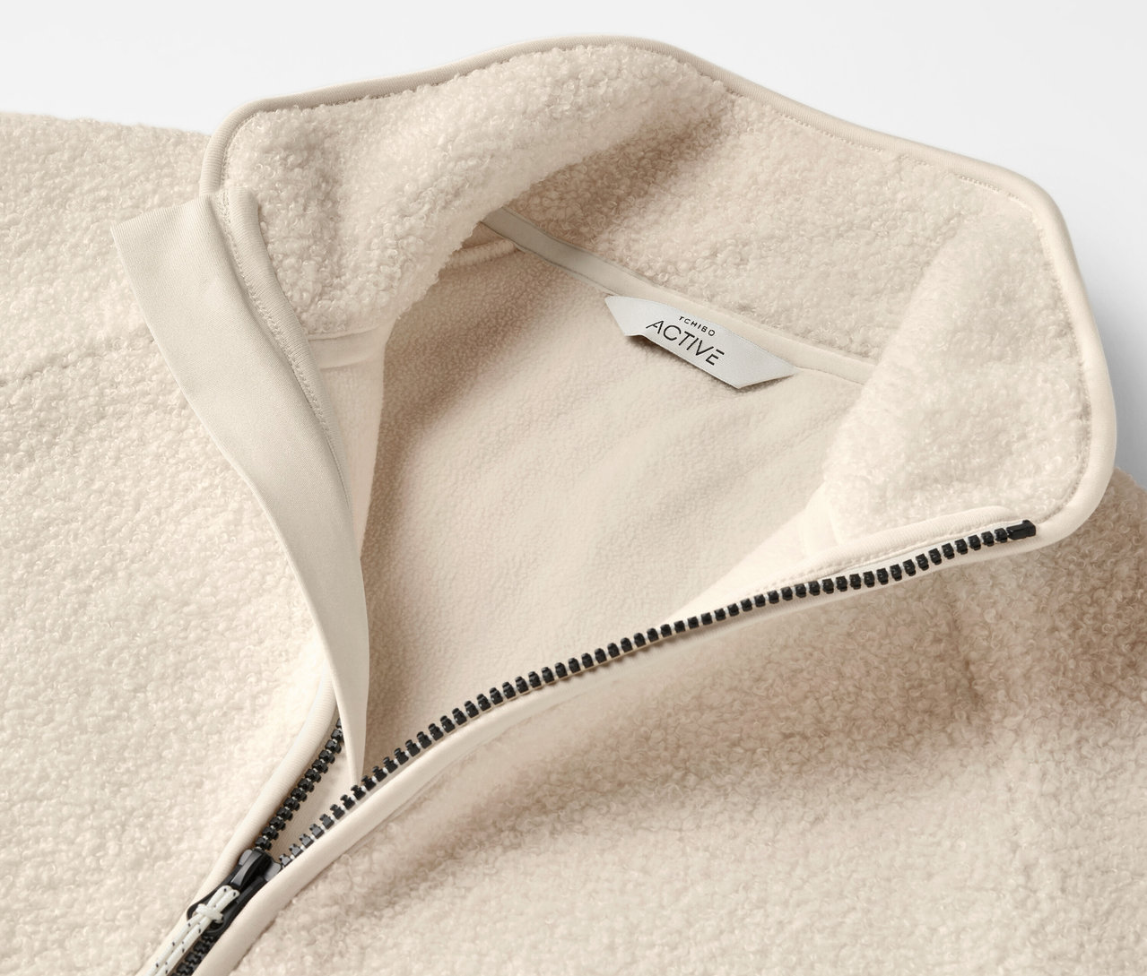 Detail béžovej flísovej mikiny so zipsom a golierom.