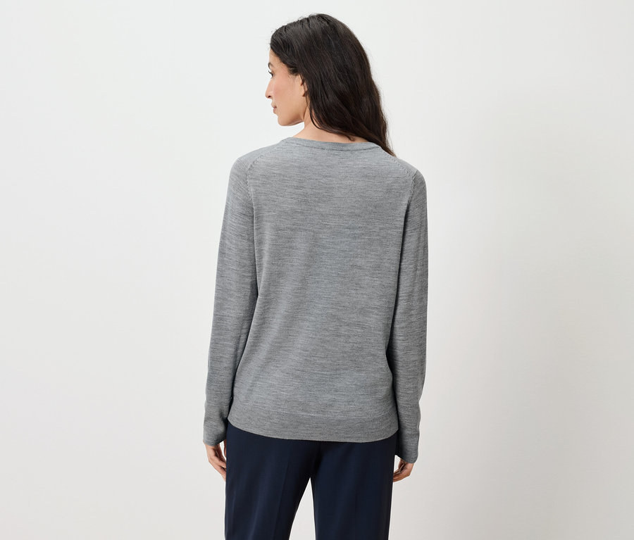 Zozadu je vidieť žena s dlhými hnedými vlasmi, ktorá má na sebe sivý sveter a tmavomodré nohavice.
