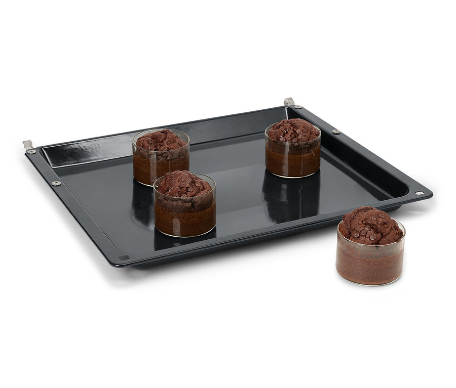 Štyri čokoládové muffiny v pohároch na čiernom plechu na pečenie.