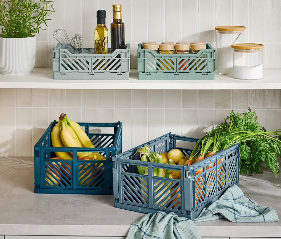 Na kuchynskej linke sú tri skladacie prepravky, jedna modrá s banánmi, jedna sivá so zeleninou a jedna sivá s kuchynskými potrebami.