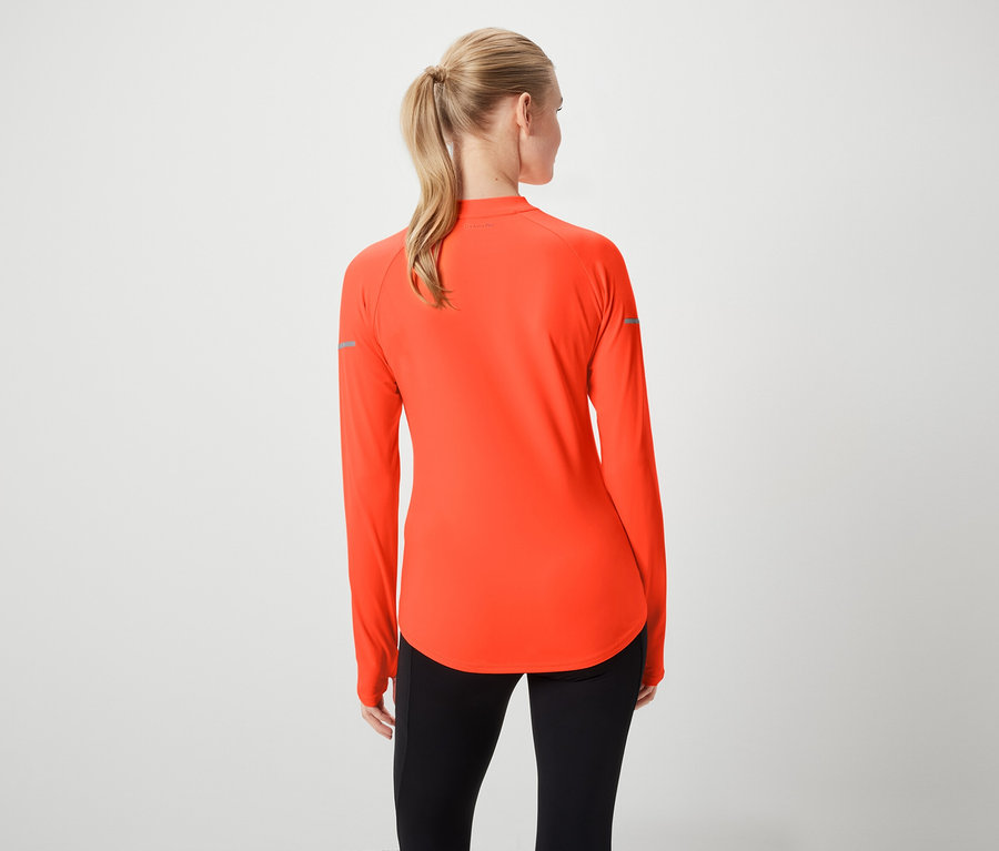 Zozadu je vidieť ženu s blond vlasmi stiahnutými do copu, má na sebe oranžovú športovú blúzku s dlhými rukávmi a čierne legíny.