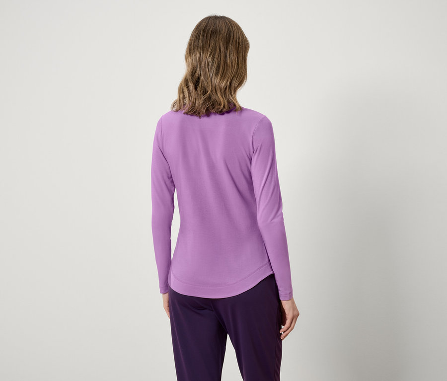 Pohľad zozadu na ženu s vlnitými vlasmi v levanduľovom tope s dlhým rukávom a fialových nohaviciach.