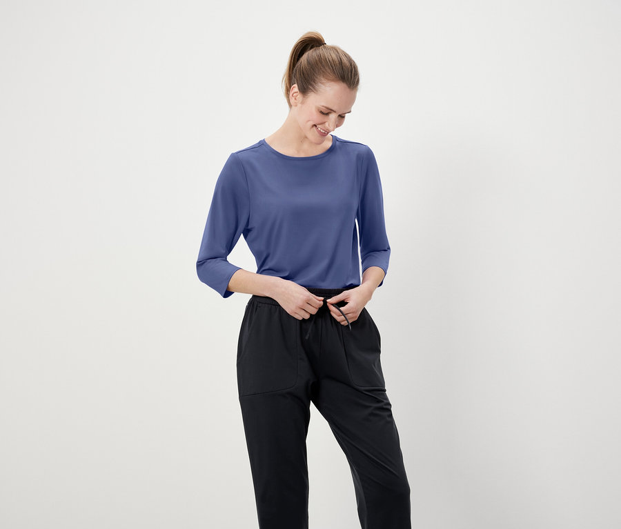 Žena si upravuje čierne nohavice s modrým tričkom s trojštvrťovým rukávom.