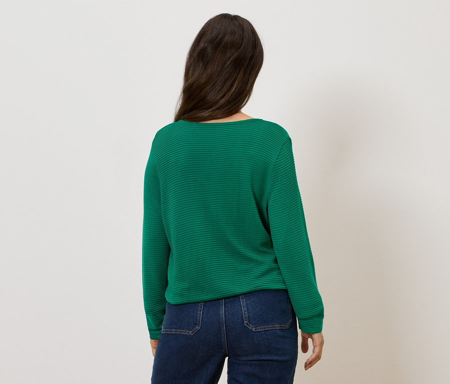 Žena stojí chrbtom a má na sebe zelený sveter a džínsy.